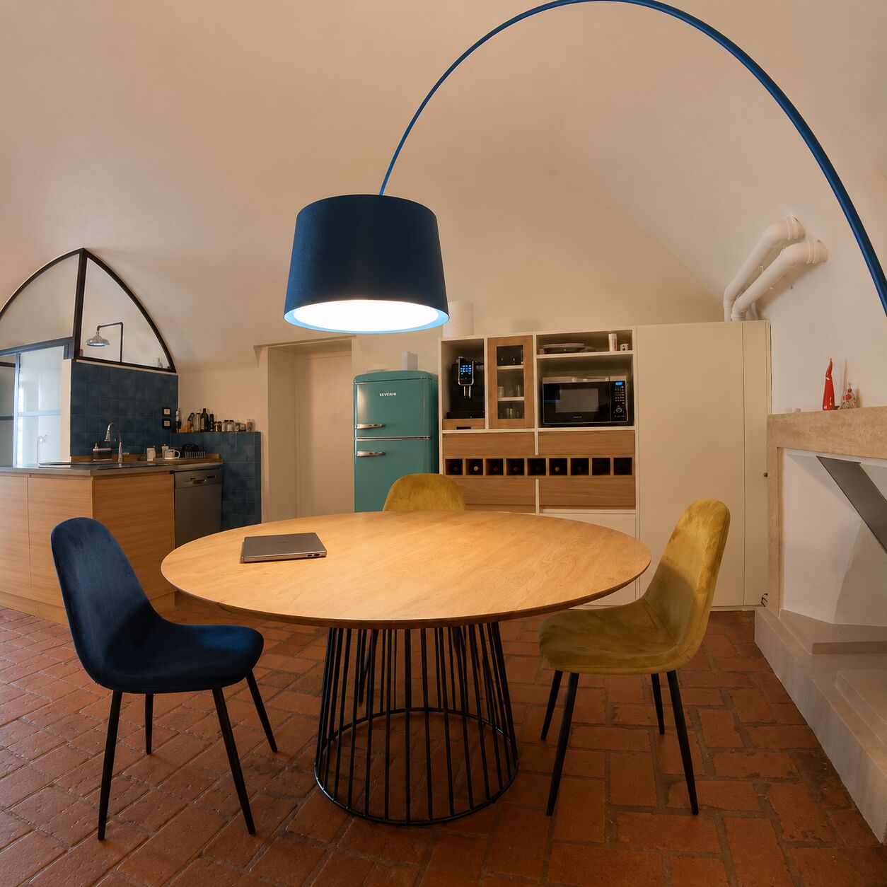 La zona pranzo sotto la volta, con la grande lampada ad arco blu e la cucina sullo sfondo