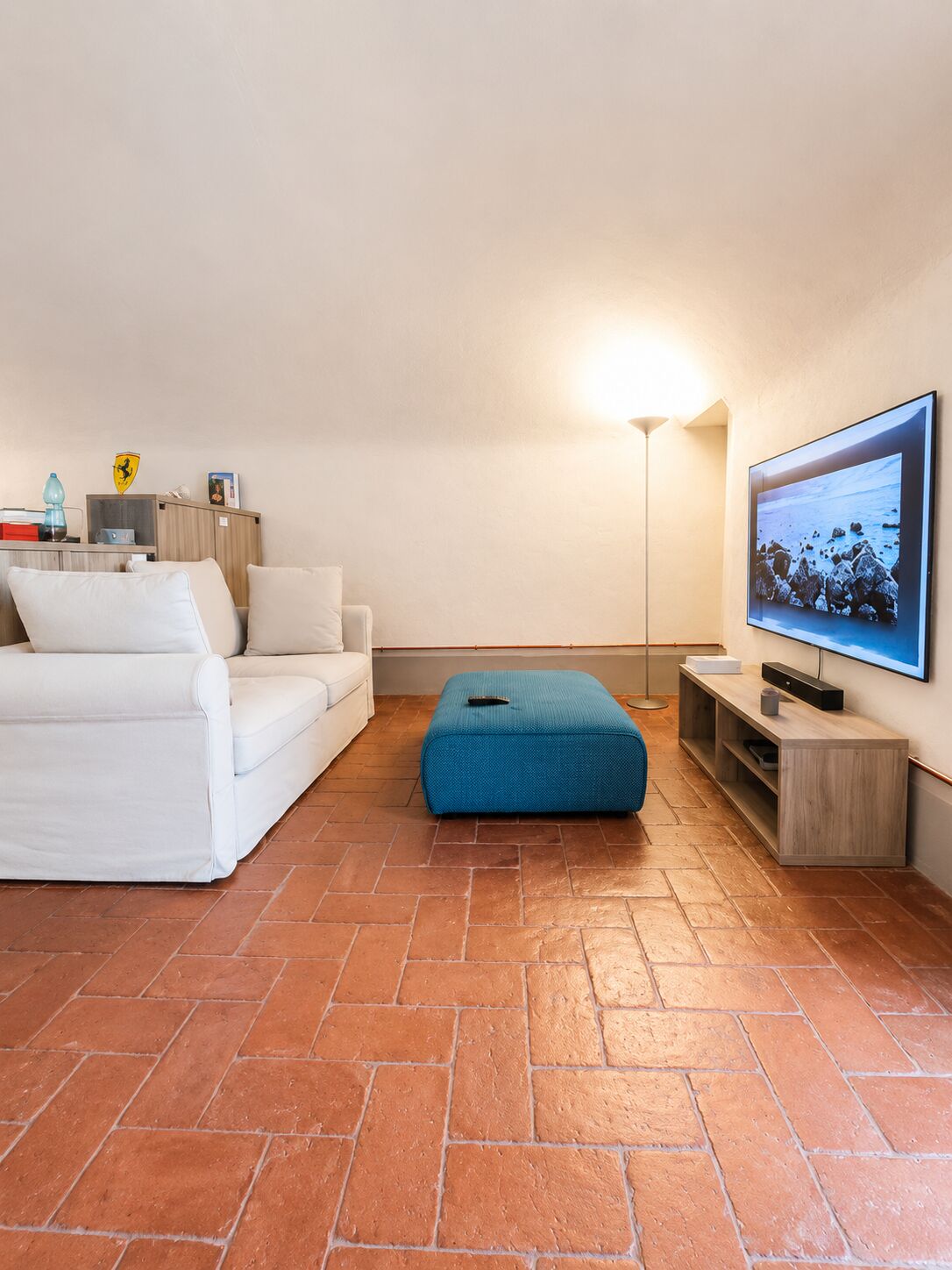 Il soggiorno con divano bianco, pouf blu e TV